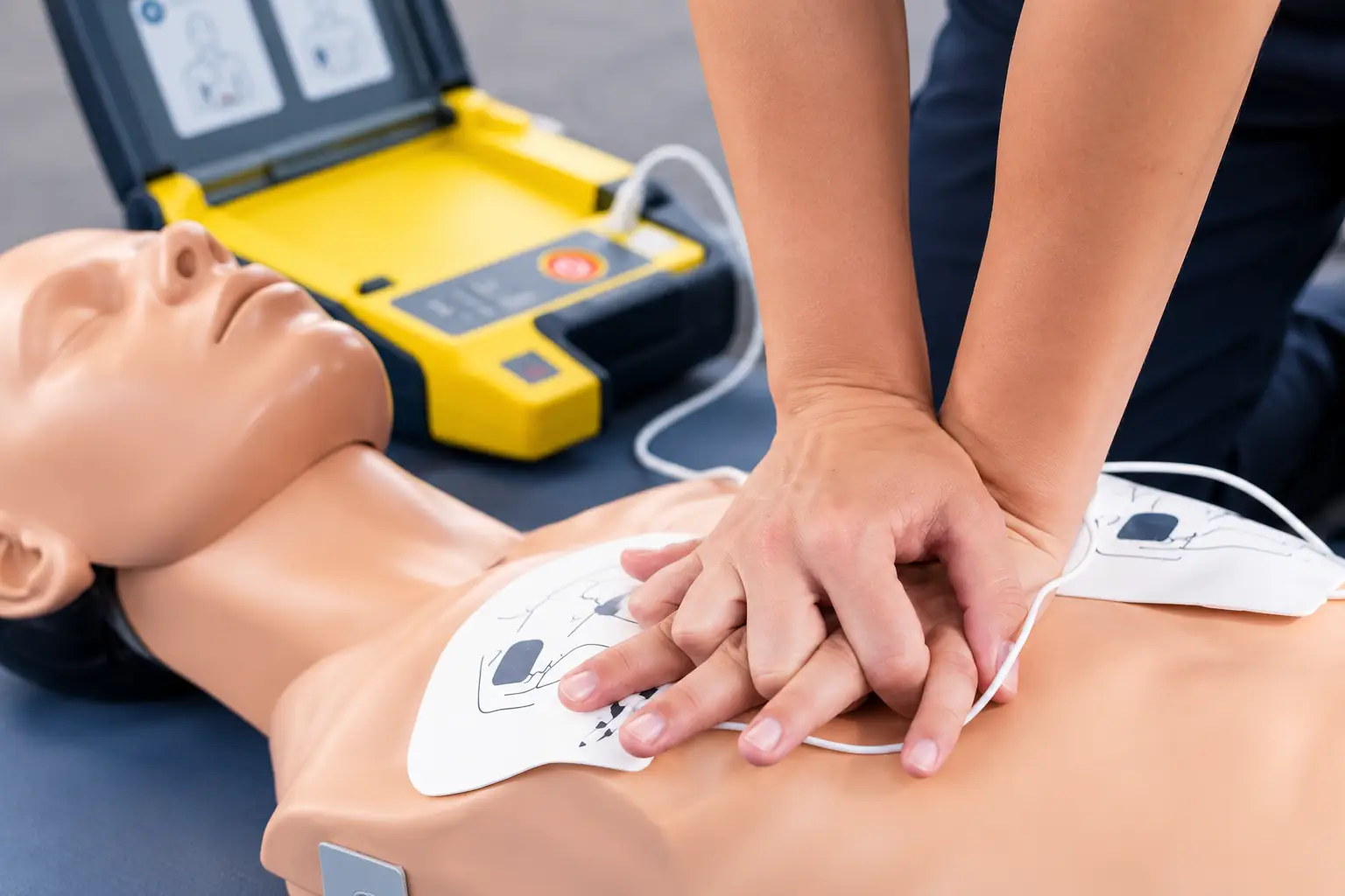 Participant practising CPR chest compressions on a training manikin with an AED